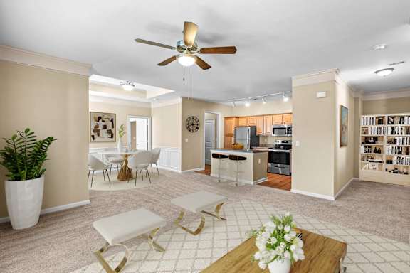 A living room with a fan, a dining table, and a kitchen in the background.