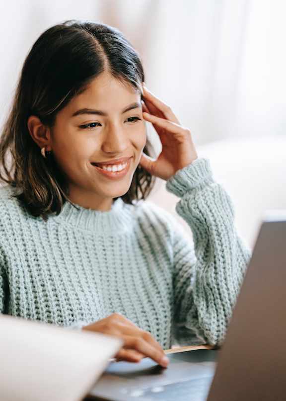 A woman in a green sweater is using a laptop and talking on the phone.