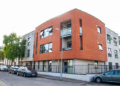 Thumbnail 1 of 6 - an apartment building on a city street with parked cars