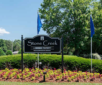 the sign for stone creek park in front of a garden with three flags