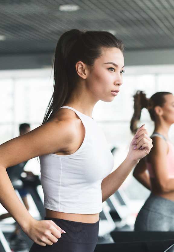 Two women are working out on treadmills in a brightly lit gym.
