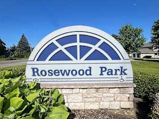a sign for rosewood park in front of a garden