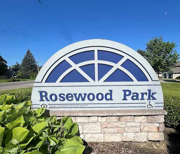 a sign for rosewood park in front of a garden