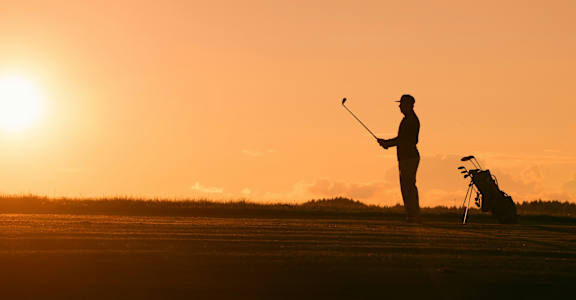 a silhouette of a man playing golf at sunset