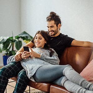 a man and woman sitting on a couch looking at a cell phone