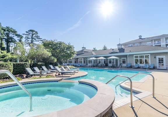 a swimming pool with lounge chairs and a hot tub with a building in the background