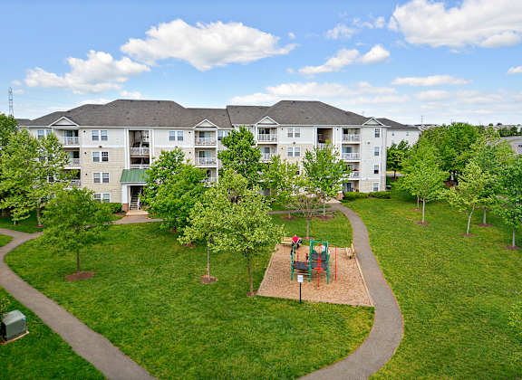 A playground with a slide is surrounded by a grassy area and trees.