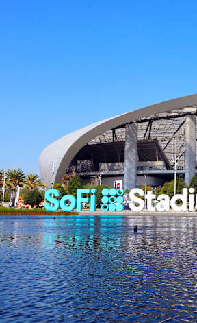A large stadium with a semi-circular roof and a body of water in the foreground.