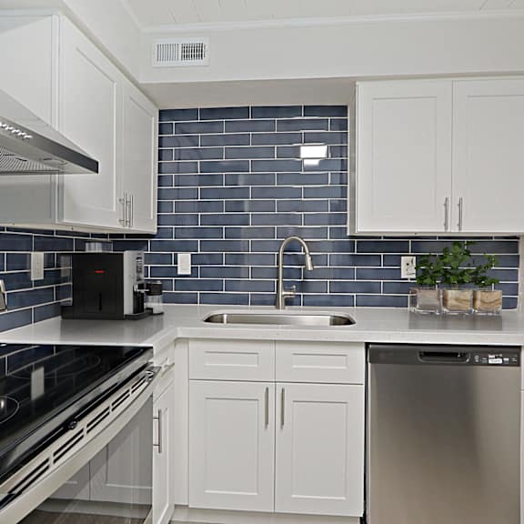 a kitchen with white cabinets and black appliances and blue subway tiles