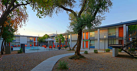 A playground area with a paved walkway and a tree in the foreground.