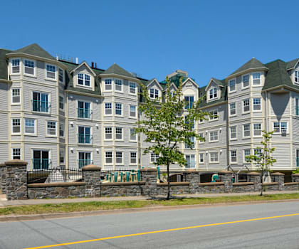 A row of apartment buildings with a stone wall and trees in front.