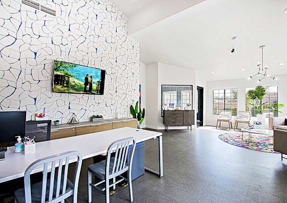 A modern office with a white desk and chairs, a television on the wall, and a patterned wallpaper.