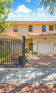 A yellow house with a black gate and a brick pathway leading to the entrance.