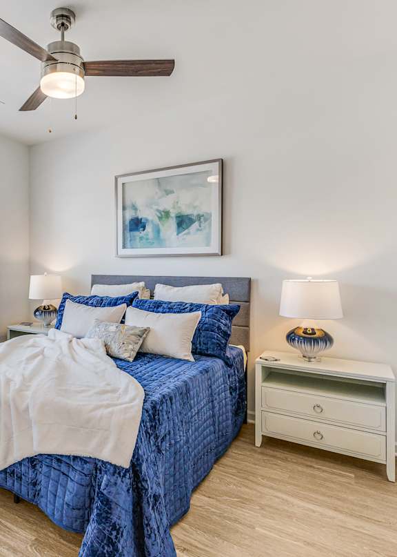 A bedroom with a blue bedspread and a ceiling fan.