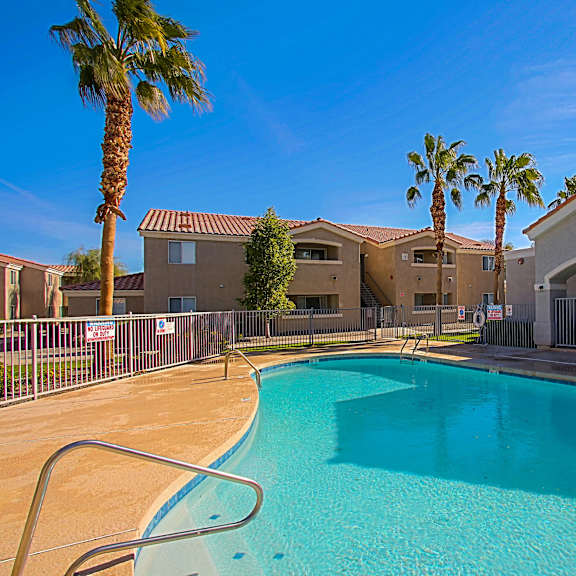 A swimming pool in front of a building with palm trees.