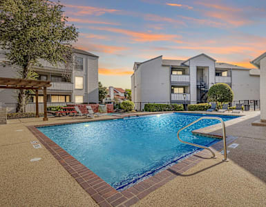 A swimming pool surrounded by a brick border and a building in the background.