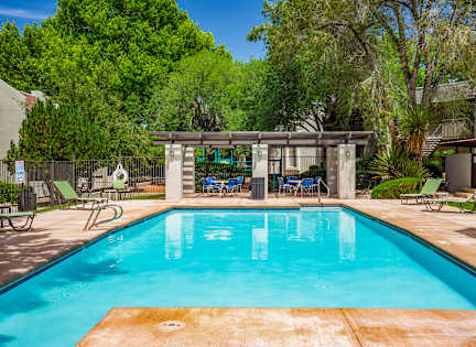 A swimming pool surrounded by trees and chairs.