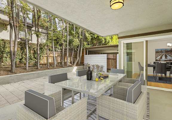 A glass table with grey chairs is in the foreground of a patio area.