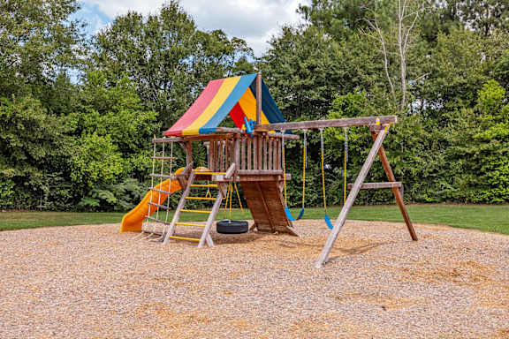 A playground with a yellow slide and a wooden swing set. at Sterlington Apartments, Grovetown, GA, 30813