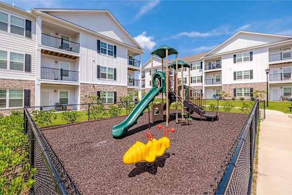A playground with a green slide and yellow slide in front of apartment buildings at The Vista Apartments & Townhomes, Warrenville, SC, 29851