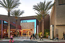 A street view of a shopping center with people walking and palm trees.