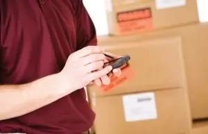 A person in a red shirt is holding a smartphone in front of cardboard boxes.