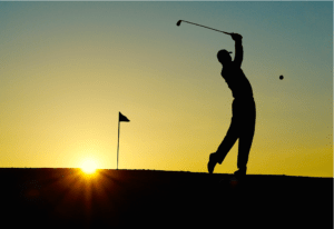 a man swinging a golf club with the sun setting in the background