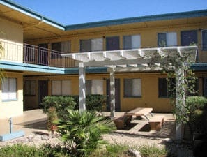 a courtyard with a pergola and a picnic table in front of a yellow building