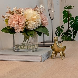 a vase with pink and white flowers on a table with a gold figurine at The Botanic, Carteret, NJ