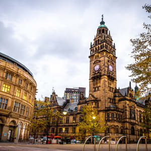 A large building with a clock tower stands in front of a cloudy sky.