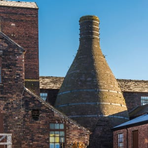 A tall brick chimney with a conical roof is in the foreground of a building.