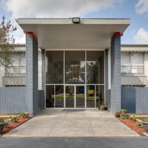 The image shows a building entrance with a glass door and a grey pillar on each side.