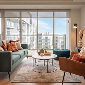 A living room with a green couch, a brown chair, a white table, and a large window with a view of buildings outside at Cherrywood Apartments, D18 VY3V, DUBLIN 18
