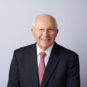An older man with glasses and a pink tie is smiling.