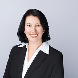 A woman with black hair wearing a black suit and white shirt.