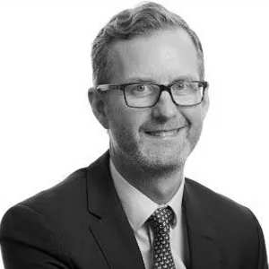 A man with glasses and a tie is smiling.