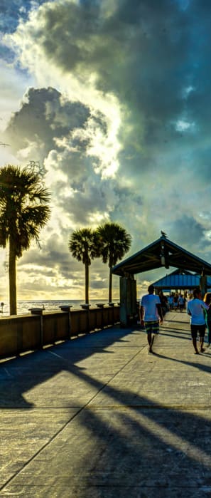 people walking down a pier at the beach with a cloudy sky