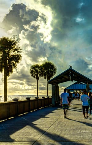 people walking down a pier at the beach with a cloudy sky