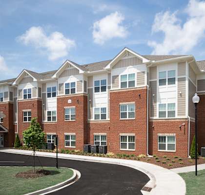 A large brick apartment building with a red car parked in front.