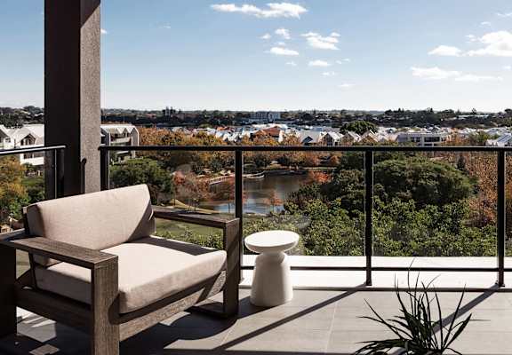 a balcony with a chair and a side table overlooking a park, lake and homes
