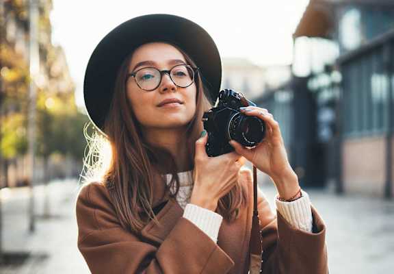 A woman in a hat and coat is taking a photo with a camera.