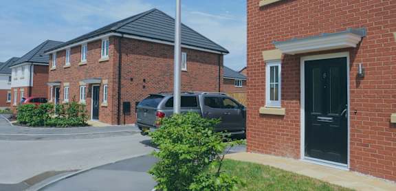 A brick house with a black door and a grey car parked in front.