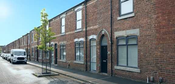 A row of red brick houses with a tree in front of the first one.