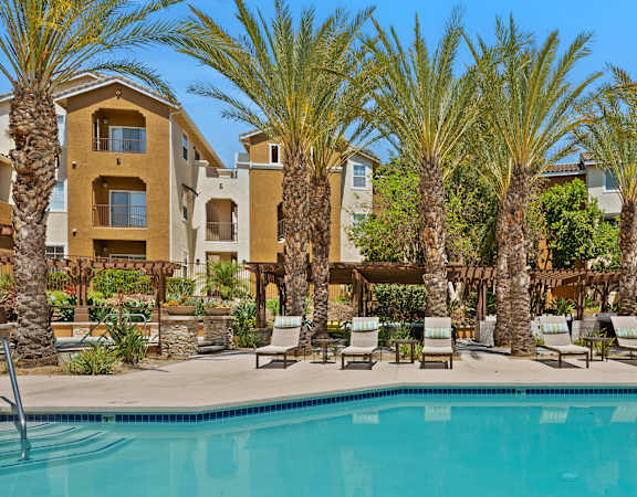 a swimming pool with chaise lounge chairs and palm trees in front of an apartment complex