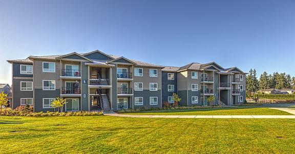 A large apartment complex with multiple balconies and a green lawn in front at GATEWAY BY VINTAGE, Spanaway