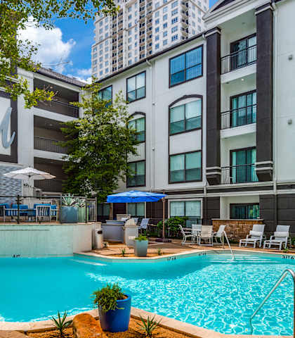 a swimming pool with chairs and umbrellas in front of an apartment building