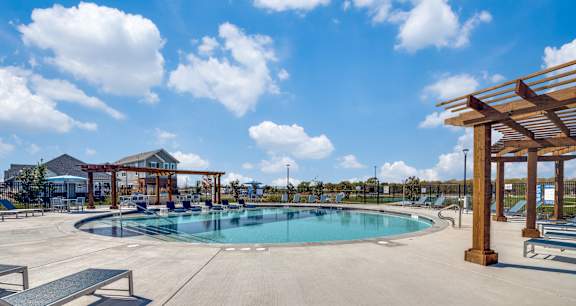 A large outdoor swimming pool with a wooden pergola and lounge chairs.