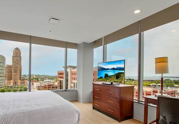 A bedroom with a large bed, a desk with a chair, and a view of the city.