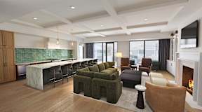 A modern living room with a fireplace and a kitchen area in the background.
