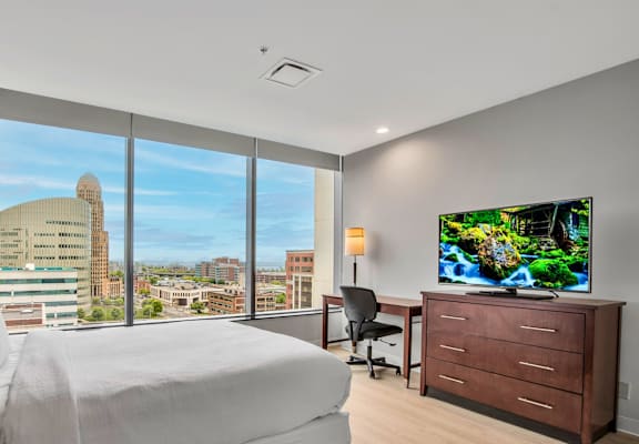 A bedroom with a large bed, a desk with a chair, and a flat-screen TV displaying a nature scene.